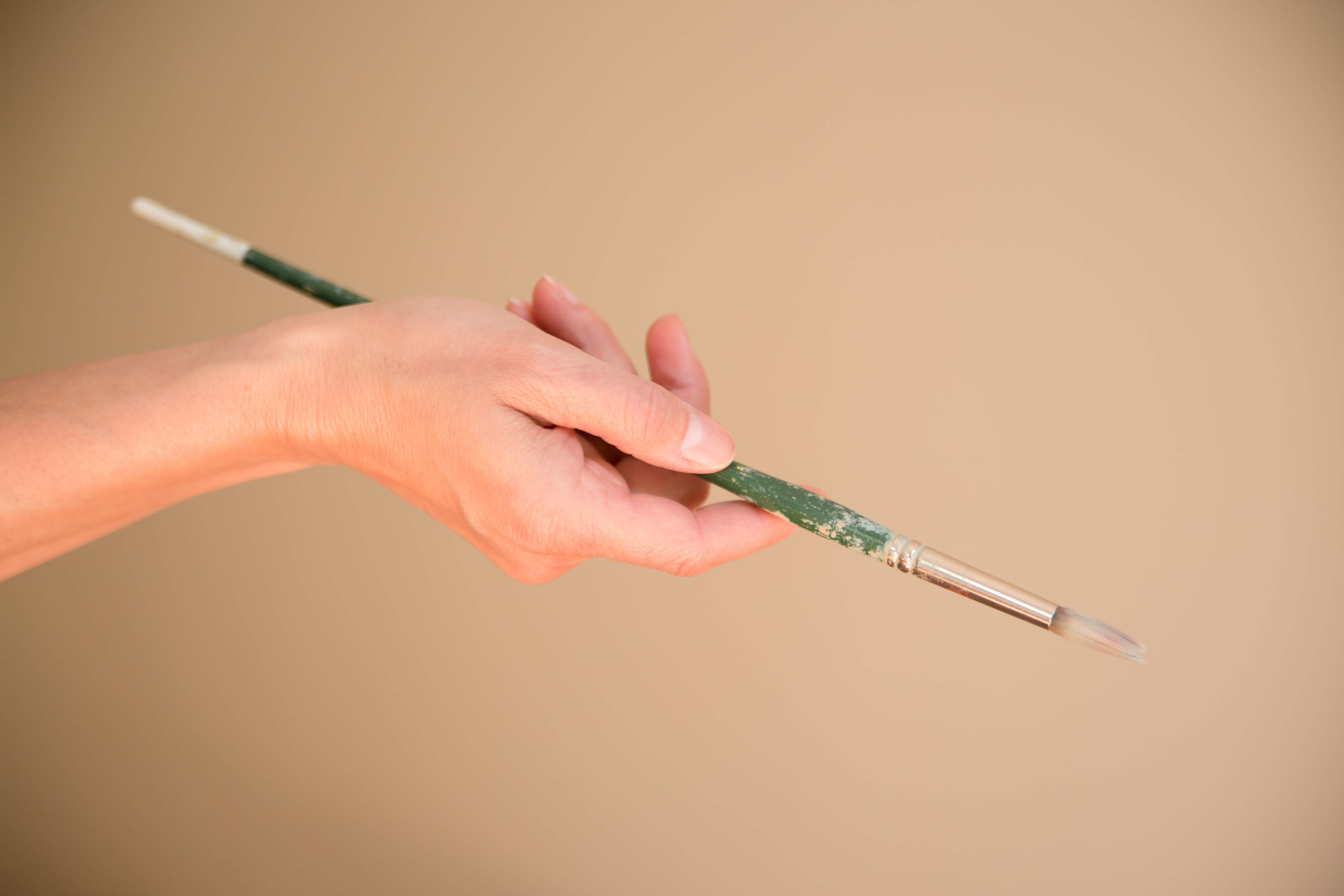 Hand holding a well-worn artist's paintbrush against a beige background